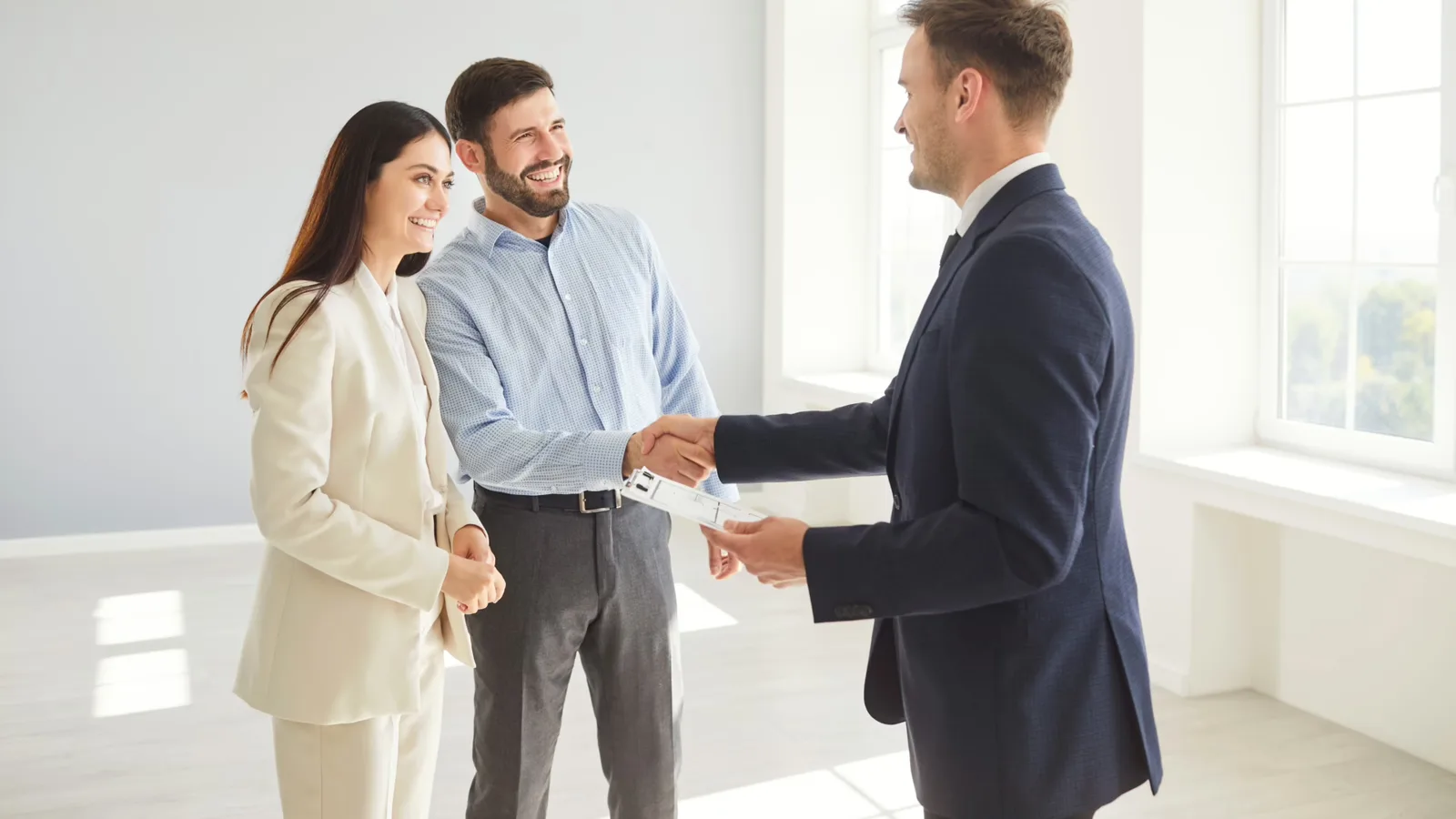 A couple shaking hands with a real estate advisor inside a bright, empty home