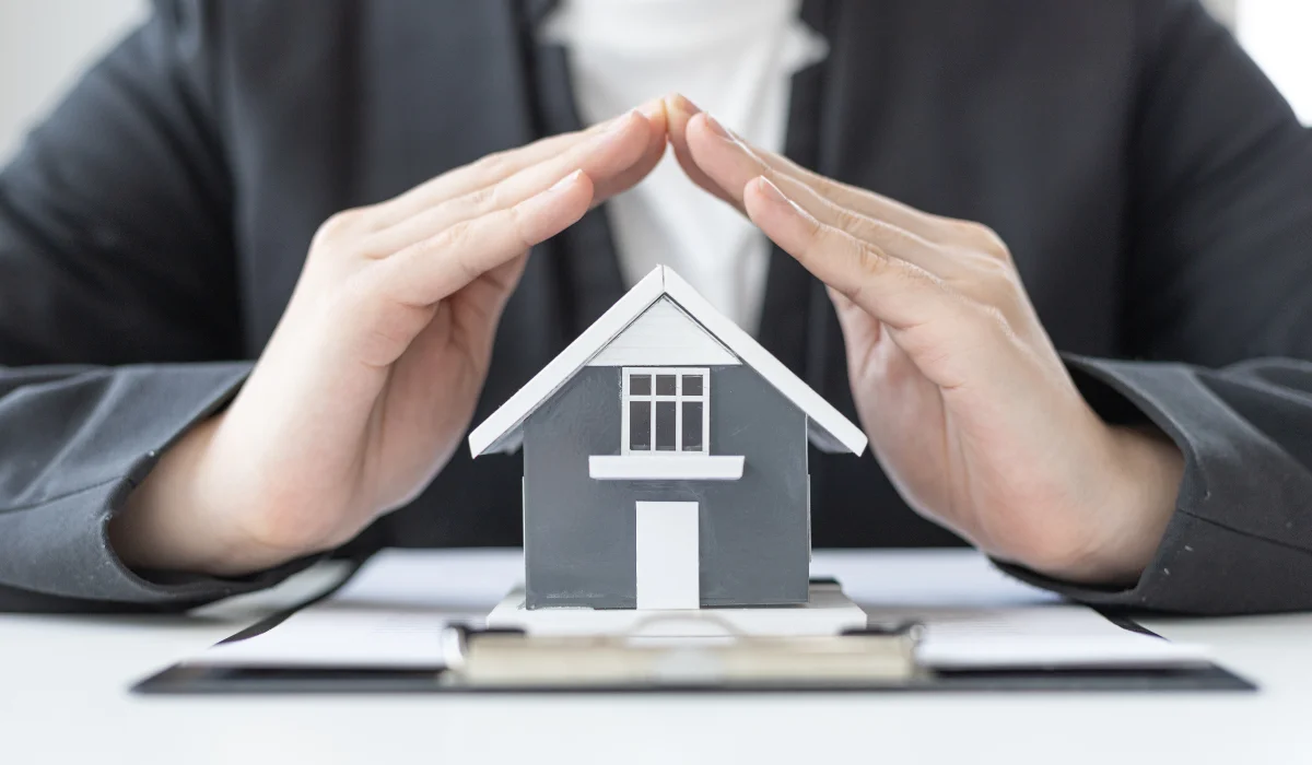 Hands sheltering a model home — protecting a rental property investment